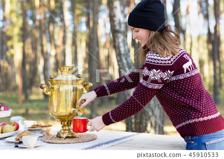 Young woman wearing jersey with hat pouring some tea using vintage russian teapot samovar 45910533