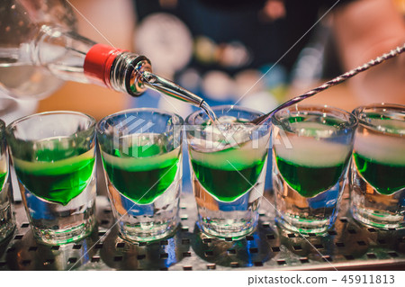 Green liquid in shot glasses standing on the counter. bartender preparing shots Green liquid in shot glasses standing on the counter. bartender preparing shots 45911813