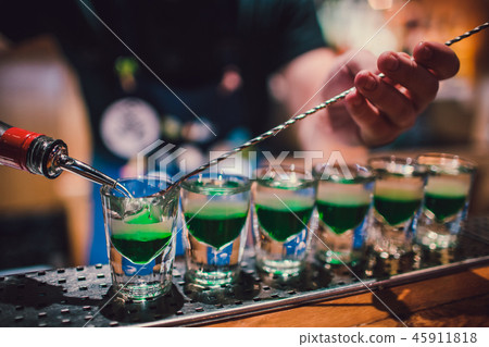 Green liquid in shot glasses standing on the counter. bartender preparing shots Green liquid in shot glasses standing on the counter. bartender preparing shots 45911818