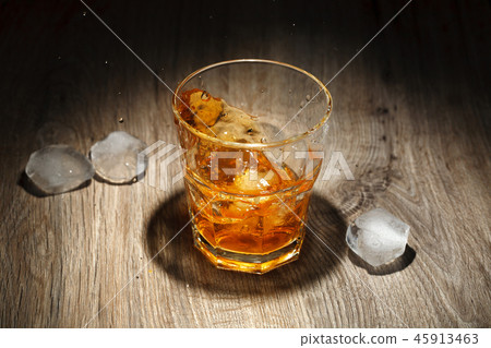 Whiskey splash in glass on a wooden table. Whiskey splash in glass on a wooden table. 45913463
