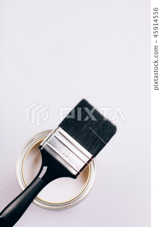 Brush with black handle on open can of white paint on grey background. Brush with black handle on open can of white paint on grey background. 45914556