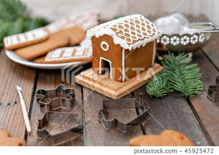 Cute little house. A lot of ginger biscuits in different form on brown wooden table. Decorated with 45925472
