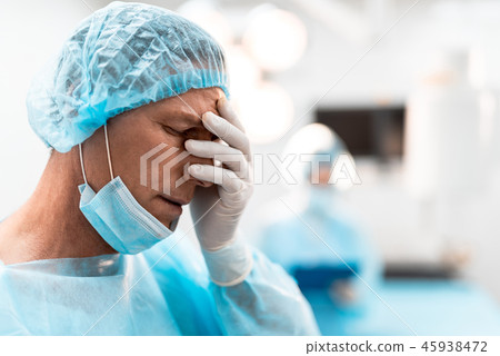 Exhausted doctor putting hand on his face while feeling tired Exhausted doctor putting hand on his face while feeling tired 45938472