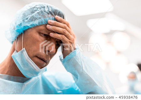 Upset doctor putting one hand on his forehead and thinking Upset doctor putting one hand on his forehead and thinking 45938476
