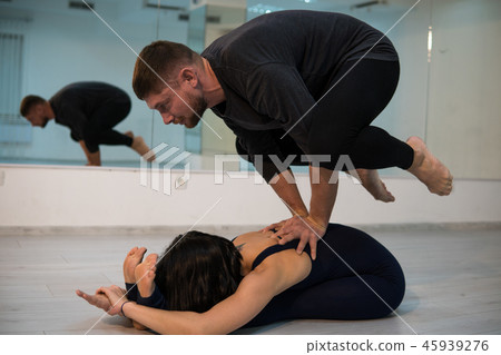 Young athletic couple in dark suits practicing acroyoga in studio with mirrors. Balancing in pair Young athletic couple in dark suits practicing acroyoga in studio with mirrors. Balancing in pair 45939276