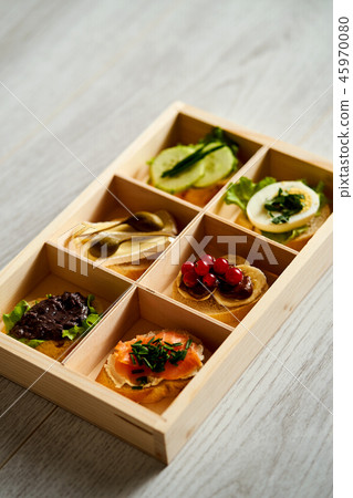 box with a set of healthy colorful mini sandwiches or tapas with vegetables and fish on a table box with a set of healthy colorful mini sandwiches or tapas with vegetables and fish on a table 45970080