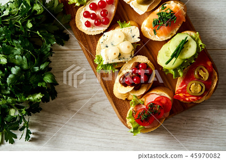 wooden board with colorful mini sandwiches or tapas along with baguette and parsley on a table wooden board with colorful mini sandwiches or tapas along with baguette and parsley on a table 45970082