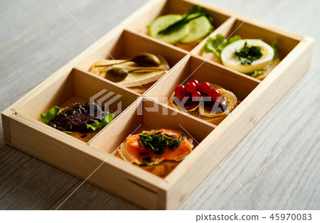 box with a set of healthy colorful mini sandwiches or tapas with vegetables and fish on a table box with a set of healthy colorful mini sandwiches or tapas with vegetables and fish on a table 45970083
