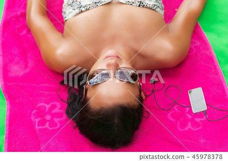 Woman on beach gets sun tan and listen music pink Woman on beach gets sun tan and listen music pink 45978378