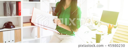 A young girl in the office sat down on the table and was holding a folder with documents. A young girl in the office sat down on the table and was holding a folder with documents. 45980230