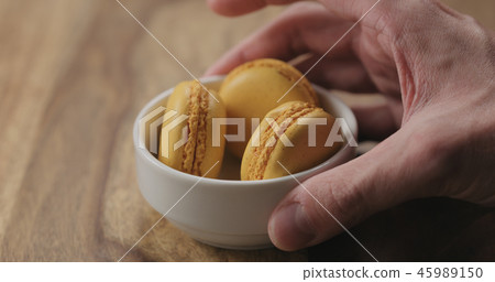 man hand put orange macarons in white bowl on wood table man hand put orange macarons in white bowl on wood table 45989150