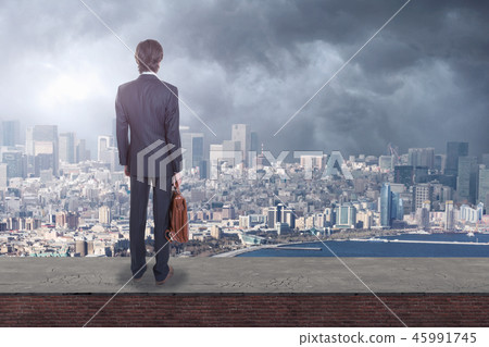 Back view of a businessman on rooftop looking at city with copy space. 45991745