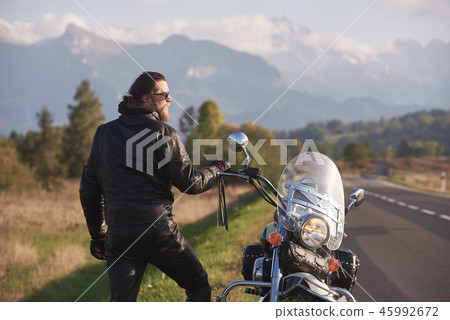 Tall athletic biker in black leather clothing standing at modern powerful high-speed motorcycle. 45992672