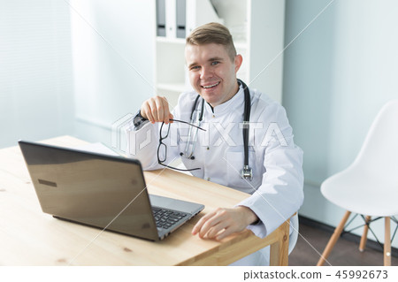 Medicine, working and people concept - doctor sitting at the table with laptop and smiling Medicine, working and people concept - doctor sitting at the table with laptop and smiling 45992673