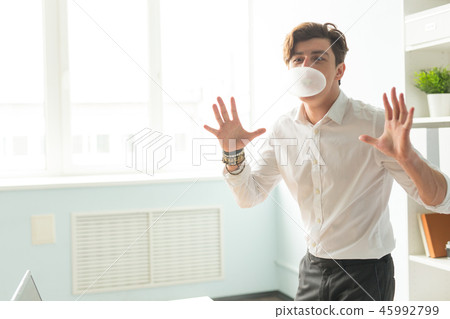 Business, fun and joke concept - young man blowing bubble of chewing gum in office Business, fun and joke concept - young man blowing bubble of chewing gum in office 45992799
