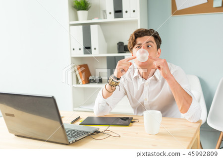 Business, fun and joke concept - young man blowing bubble of chewing gum in office Business, fun and joke concept - young man blowing bubble of chewing gum in office 45992809