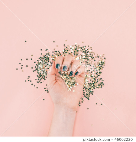 Woman hands covered golden stars confetti on pink Woman hands covered golden stars confetti on pink 46002220
