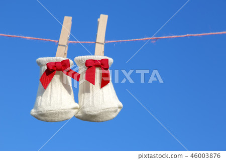 與紅色絲帶的新出生的襪子在木曬衣夾垂懸了反對藍天。嬰兒,育兒,分娩,幸福,愛情形象 與紅色絲帶的新出生的襪子在木曬衣夾垂懸了反對藍天。嬰兒,育兒,分娩,幸福,愛情形象 46003876
