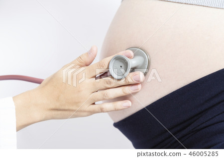A close-up of a female doctor who examines a pregnant woman's big belly with a stethoscope. Pregnancy, medical examination, last month, examination, obstetrics and gynecology department, female doctor image 46005285