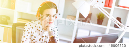 Beautiful young girl sitting in headphones and with microphone at table in office and talking. 46006310