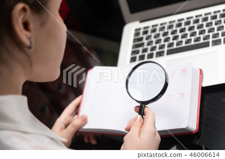 Young businesswoman with magnifying glass looking at diary on laptop background Young businesswoman with magnifying glass looking at diary on laptop background 46006614