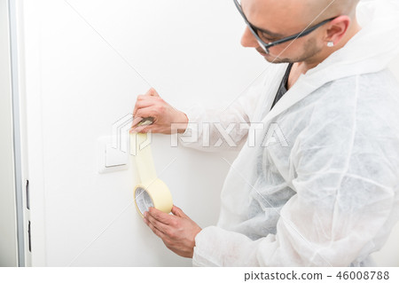 Professional painter sticking the tape near the switch Professional painter sticking the tape near the switch 46008788