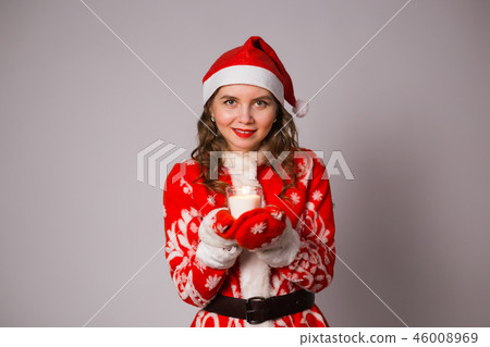 Christmas, celebration, people concept - Young charming woman in a Santa suit is holding a candle Christmas, celebration, people concept - Young charming woman in a Santa suit is holding a candle 46008969