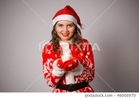 Christmas, celebration, people concept - Young charming woman in a Santa suit is holding a candle Christmas, celebration, people concept - Young charming woman in a Santa suit is holding a candle 46008970
