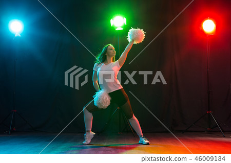Cheerleading young woman dancing with pom-poms on colourful background Cheerleading young woman dancing with pom-poms on colourful background 46009184