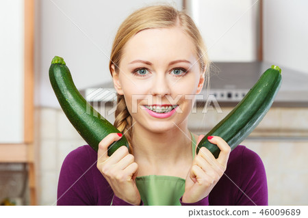 Woman in kitchen holds zucchini vegetable 46009689