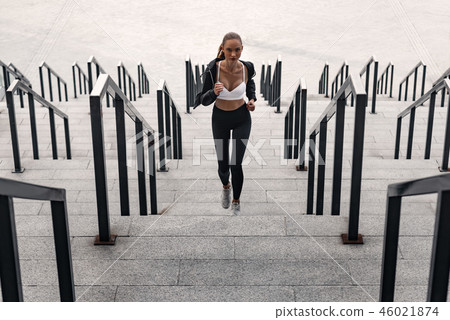 Sporty young woman is running upstairs outdoors. Front view 46021874