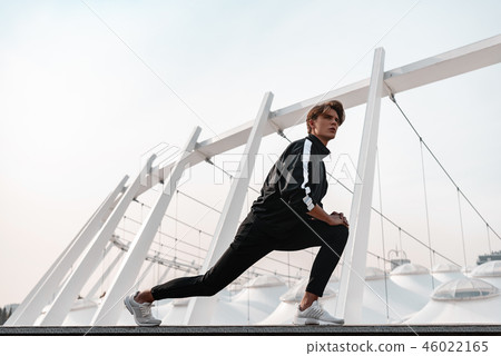 Young man is doing warming up exercises near the stadium 46022165