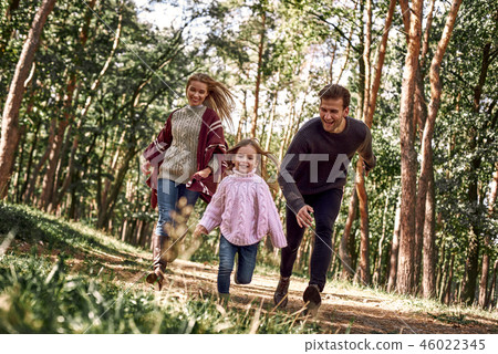 Happy parents with their daughter hold hands and run at forest path Happy parents with their daughter hold hands and run at forest path 46022345