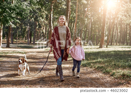 Mother and daughter with dog walking in pine forest Mother and daughter with dog walking in pine forest 46023002