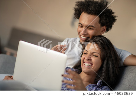 Cheerful happy African American young marriage laughing while watching movie on laptop computer at Cheerful happy African American young marriage laughing while watching movie on laptop computer at 46028689