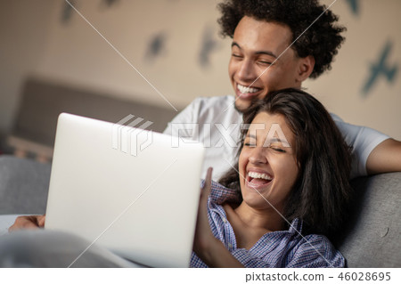 Cheerful happy African American young marriage laughing while watching movie on laptop computer at Cheerful happy African American young marriage laughing while watching movie on laptop computer at 46028695