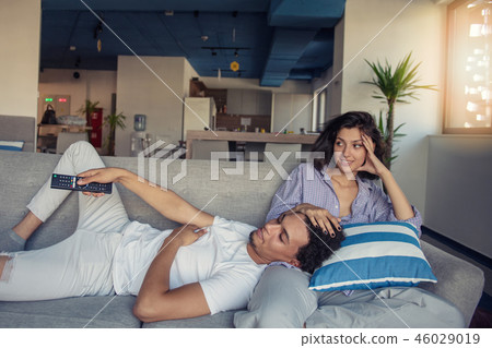 Image of smiling couple sitting on floor near sofa at home and looking aside while eating popcorn Image of smiling couple sitting on floor near sofa at home and looking aside while eating popcorn 46029019