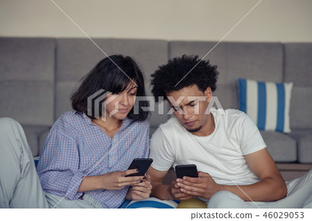 Relaxed couple or friends using a generic mobile phone together sitting on a sofa in the living room 46029053