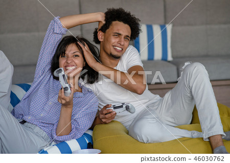 Playful young couple playing video games in their living room. 46030762