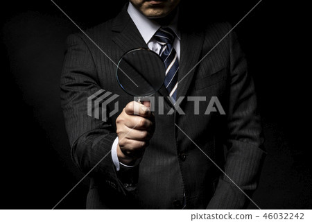 一個男人穿著西裝用放大鏡在他的手中 一個男人穿著西裝用放大鏡在他的手中 46032242