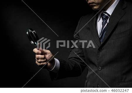 A man in a suit with a magnifying glass in his hand A man in a suit with a magnifying glass in his hand 46032247