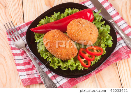 two fried breaded cutlet with lettuce on a black plate and wooden background two fried breaded cutlet with lettuce on a black plate and wooden background 46033431