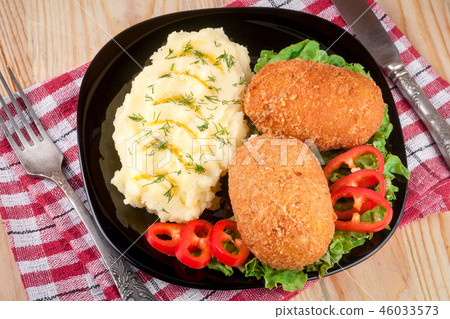 two fried breaded cutlet with mashed potatoes and lettuce on a black plate  wooden background 46033573