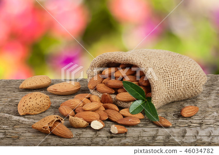 Almonds with leaf in bag from sacking on a wooden table with blurred garden background 46034782