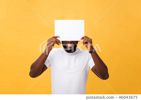 Young happy African-american hiding behind a blank paper, isolated on yellow background 46043675