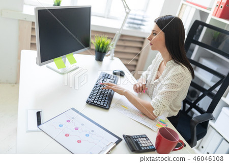 A young girl working in the office with documents and a computer. Portrait of a young girl at the A young girl working in the office with documents and a computer. Portrait of a young girl at the 46046108