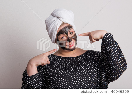 An attractive overweight woman with black facial mask on her face in a studio. 46046209