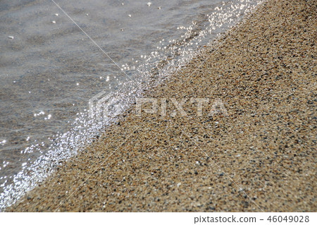 A calm beach. A sparkling sea surface reflecting sunlight. 46049028