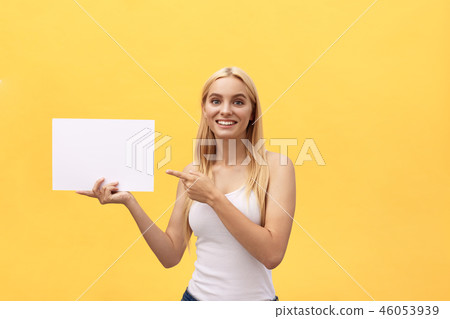 Young woman over yellow background holding blank paper sheet with surprise face pointing finger copy Young woman over yellow background holding blank paper sheet with surprise face pointing finger copy 46053939