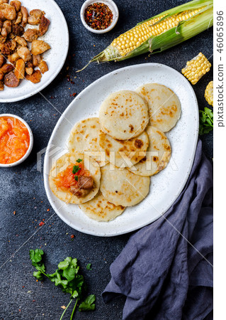 COLOMBIAN FOOD. Maize AREPAS and fried pork chicharron ans colombian tomato sauce. Top view. Black COLOMBIAN FOOD. Maize AREPAS and fried pork chicharron ans colombian tomato sauce. Top view. Black 46065896